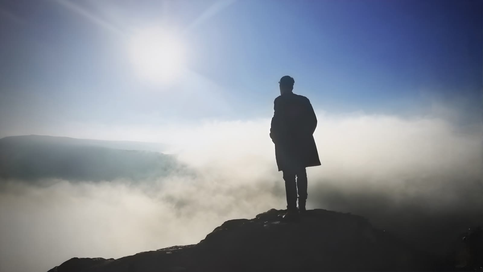 Silhouette standing above sunlit fog